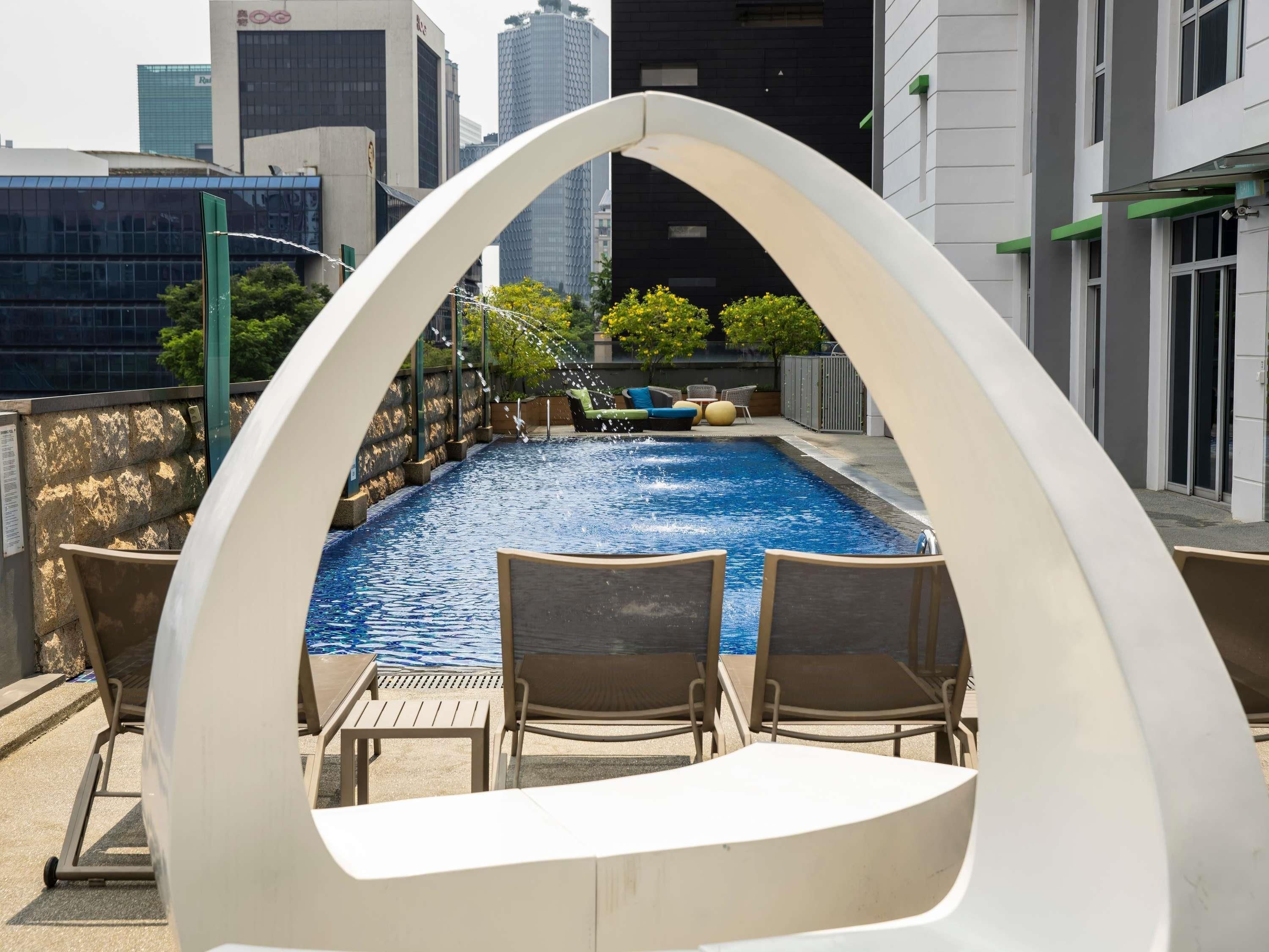 Un área de piscina en la azotea con vista al horizonte de la ciudad, rodeada de edificios modernos.