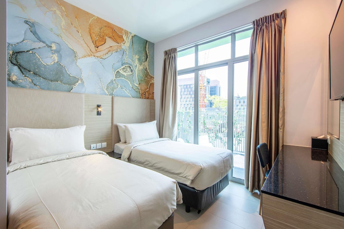 A hotel room with two beds, a large window with curtains, a desk, and a wall with a marble-like design.