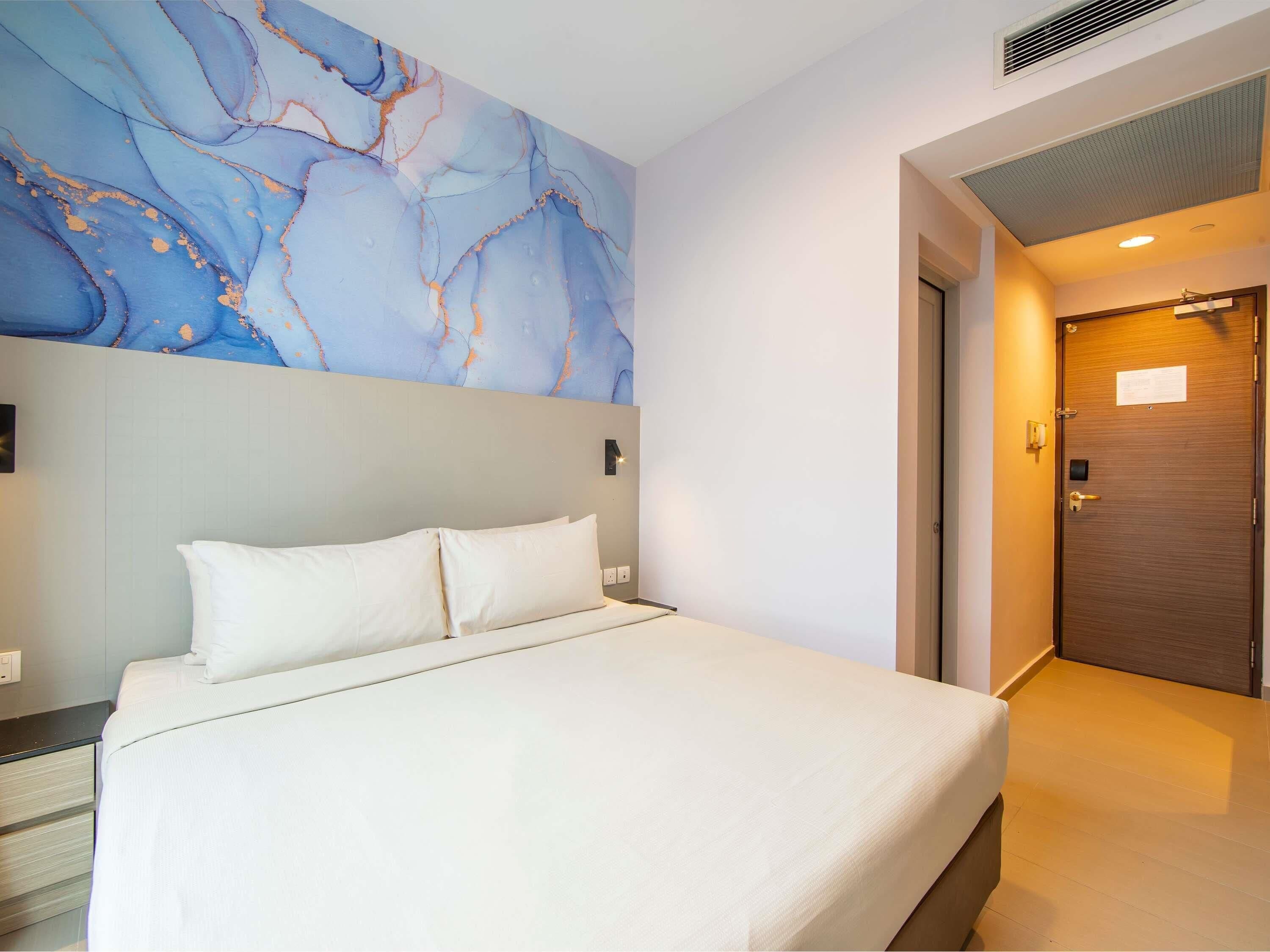 Une chambre d’hôtel avec un lit, un mur en marbre, une porte en bois et un interrupteur.