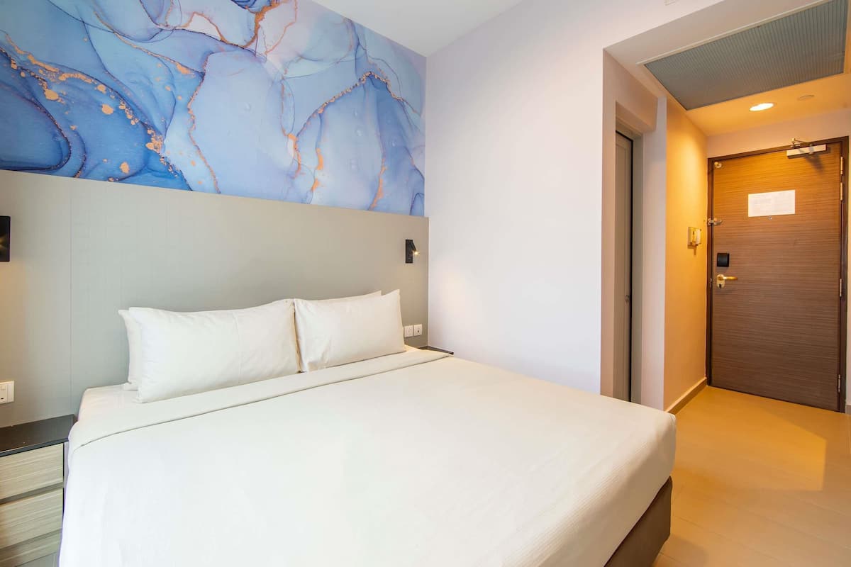 Quarto de hotel com cama, parede de mármore, porta de madeira e interruptor de luz.