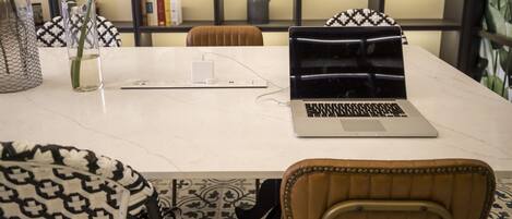 A modern workspace with a laptop on a marble table, surrounded by patterned chairs and a potted plant.