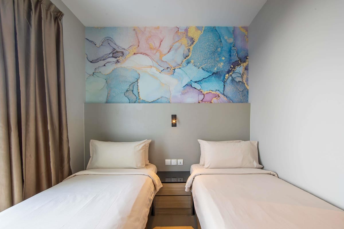 A hotel room with two beds, a large abstract painting on the wall, and a window with curtains.