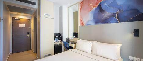 A hotel room with a bed, a desk, a chair, a mirror, and a wall with a colorful abstract design.