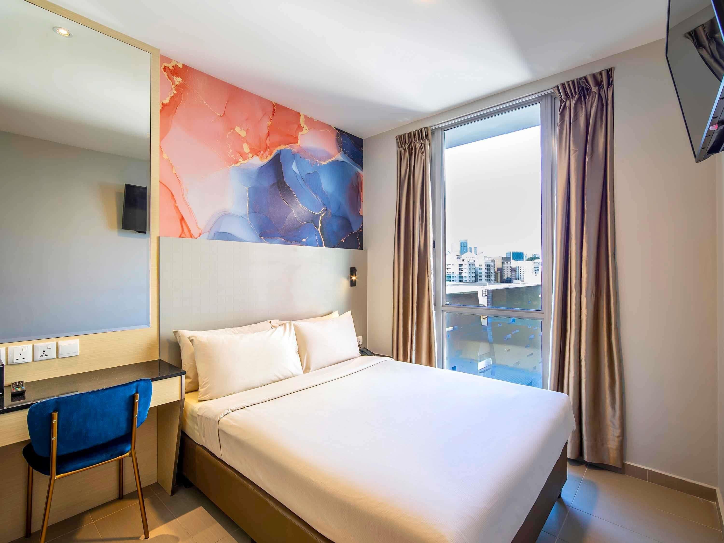 Une chambre d’hôtel avec un lit, un bureau, une chaise, une grande fenêtre avec des rideaux et une vue sur la ville.