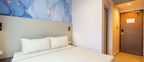 A hotel room with a bed, a marble wall, a wooden door, and a light switch.