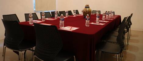 A conference room with a long table, black chairs, water bottles, name cards, and a decorative vase.