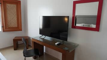 Une chambre moderne avec un téléviseur à écran plat posé sur un bureau en verre, un petit tabouret en bois et un miroir avec un cadre rouge.