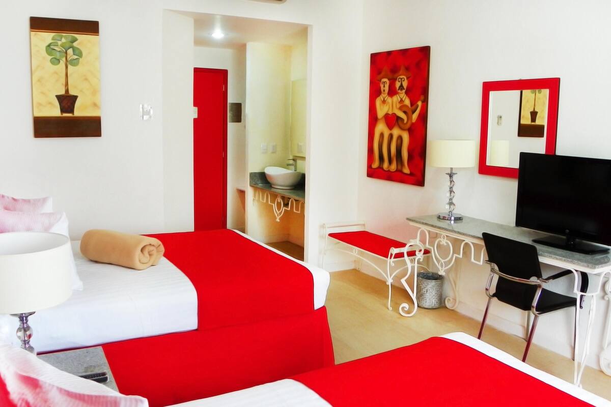 A hotel room with a bed, desk, TV, and artwork on the walls.