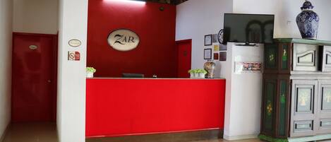 A reception area with a red counter, a sign that reads "ZAR," and a large decorative vase on a cabinet.