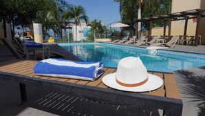 Ett område vid poolen med solstolar, en pool och ett bord med en handduk och en hatt.