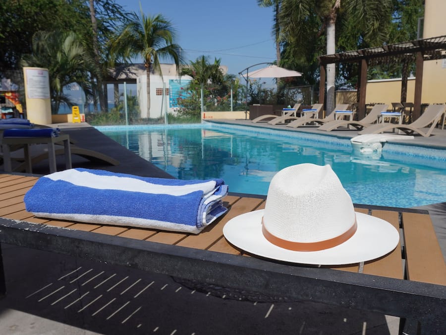 A poolside area with lounge chairs, a pool, and a table with a towel and hat.
