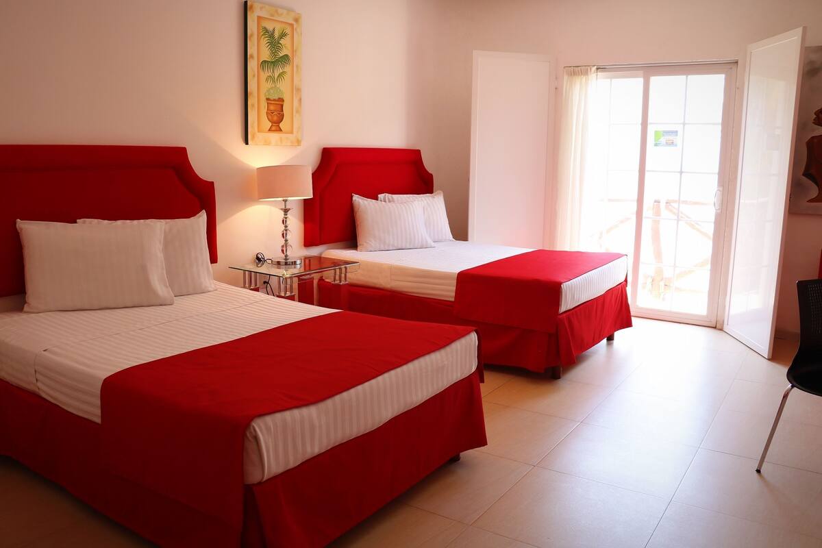A hotel room with two beds, a nightstand, a lamp, and a door leading to a balcony.