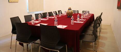 A conference room with a red table, black chairs, water bottles, and a decorative vase.
