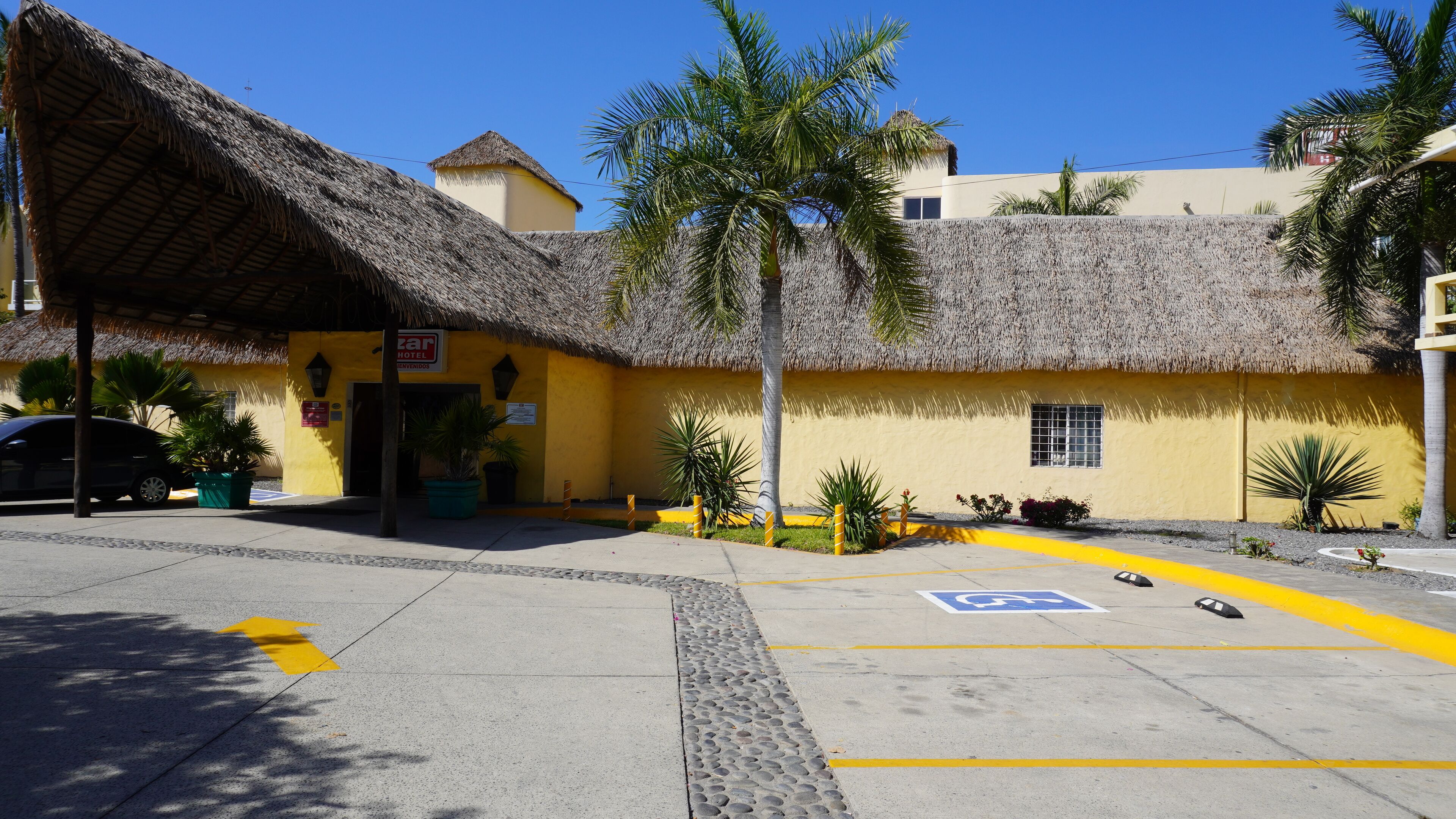 A hotel with a thatched roof, yellow walls, and a parking area with a handicapped parking sign.