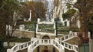 A grand staircase with white balustrades and a central arched entrance, surrounded by lush greenery and stone walls. - Mondial Appartement Hotel (Vienna)