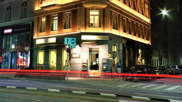 A corner building with a ground-floor entrance, multiple windows, and a sign indicating a business on the ground floor. - Mondial Appartement Hotel (Vienna)