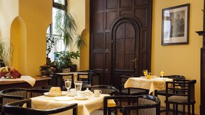 A dining area with tables set for two, featuring white tablecloths and dark wooden chairs. - Mondial Appartement Hotel (Vienna)