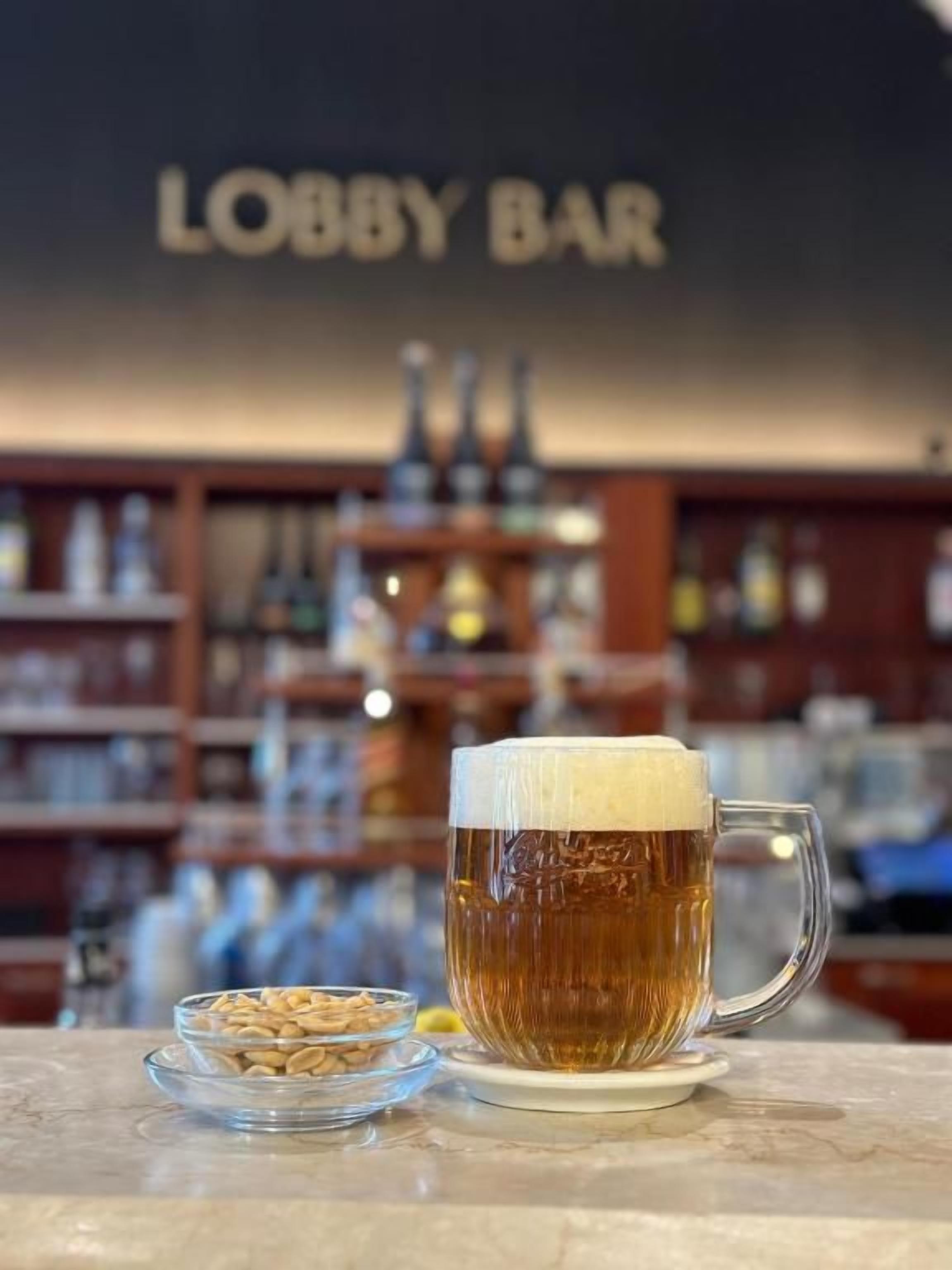 Um bar com uma garrafa de cerveja, uma tigela de petiscos e uma placa ao fundo com a inscrição 'Lobby Bar'.