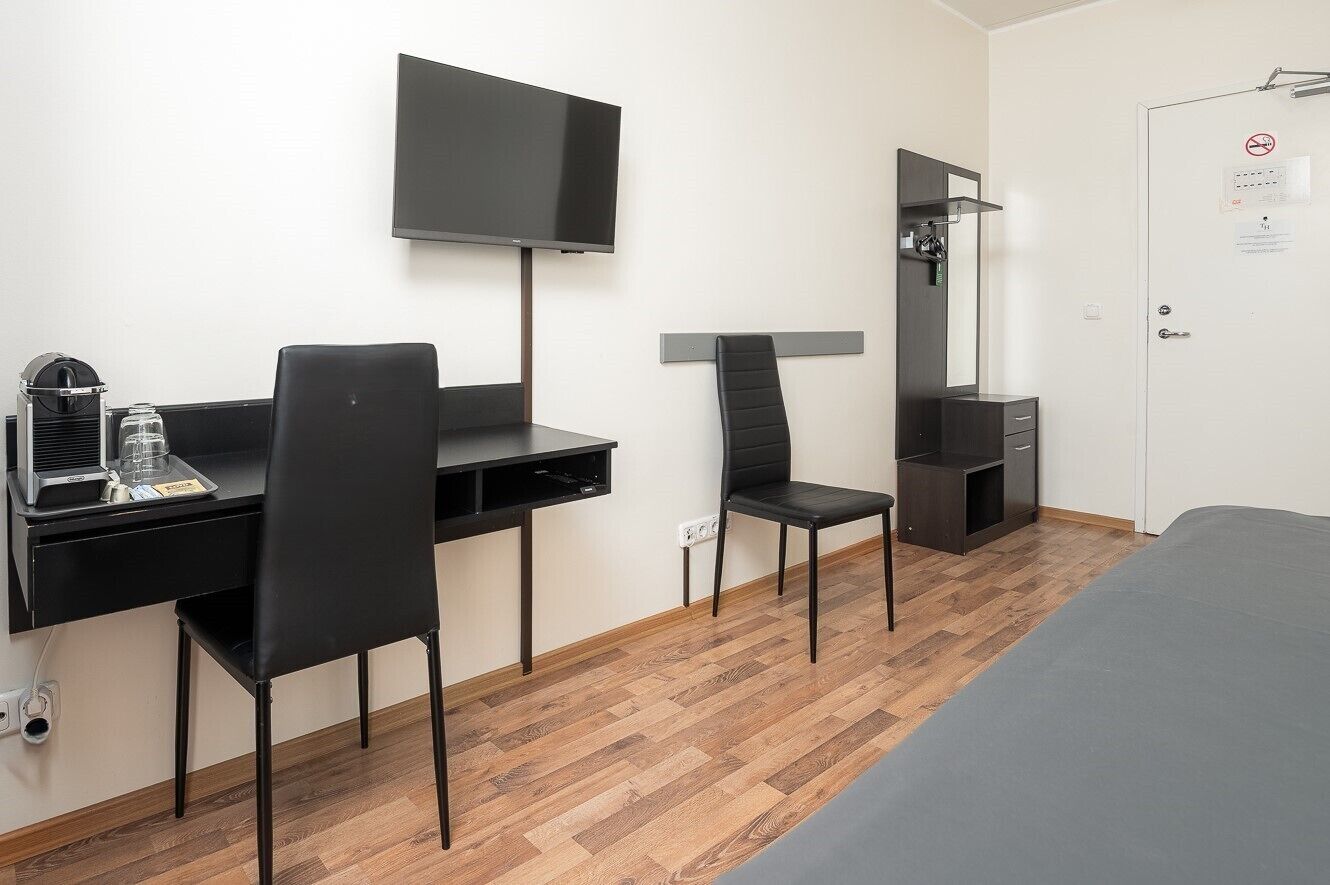 Een hotelkamer met een bed, een bureau met stoel, een televisie, een spiegel en een kledingkast.