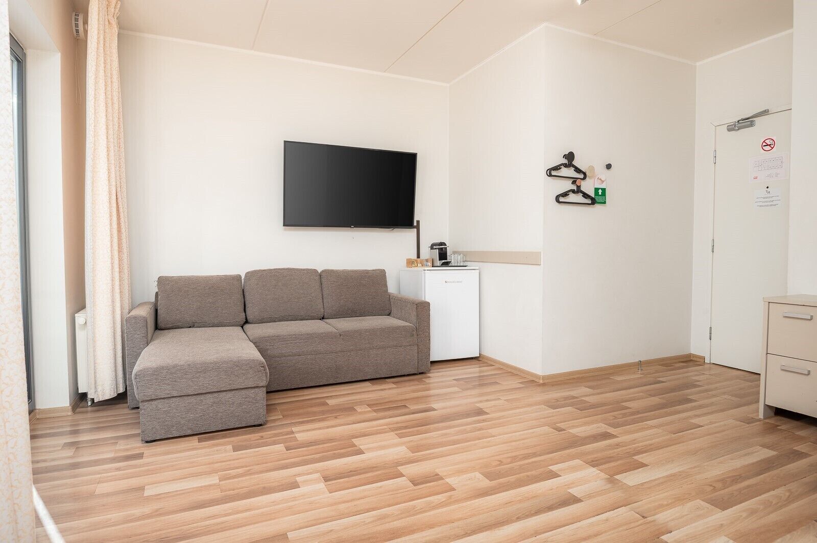 A modern living room with a sofa, a flat-screen TV, a coffee machine, and a small white cabinet.