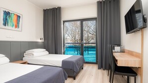 A hotel room with two beds, a desk, a TV, and a balcony with a view of the water. - Hotell Tammsaare Full Automated Hotel (Parnu)