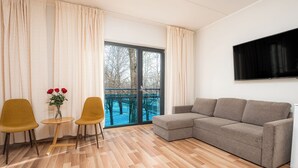 A modern living room with a sectional sofa, two yellow chairs, a small table with a vase of red roses, and a large window with a view of trees. - Hotell Tammsaare Full Automated Hotel (Parnu)