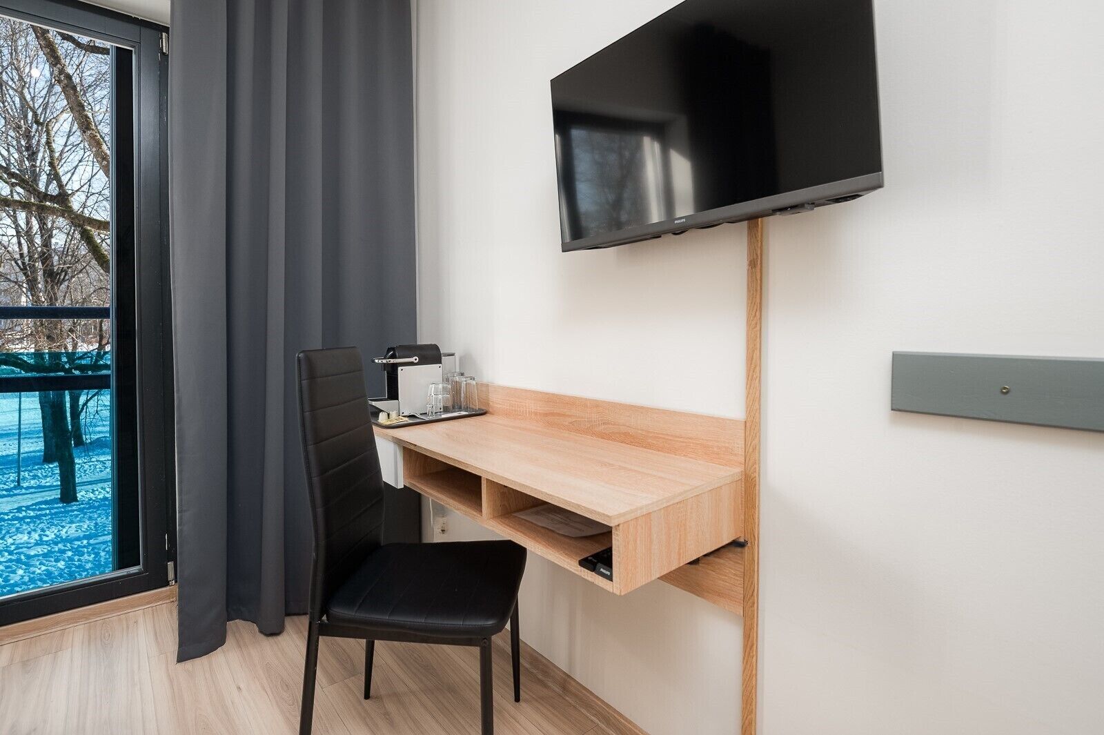 Una habitación moderna con escritorio, silla, televisión y ventana con cortinas.