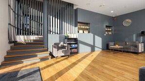 A modern interior with a staircase, grey sofa, wooden flooring, and a bookshelf. - Hotell Tammsaare Full Automated Hotel (Parnu)