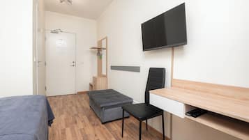 A small, modern room with a bed, a desk, a chair, a television, and a small bench.