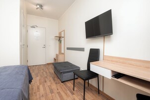 A small, modern room with a bed, a desk, a chair, a television, and a small bench.