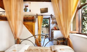 Ein Schlafzimmer mit Bett, Vorhängen, einem Fenster, einem Fernseher und einem Balkon mit Blick auf Grünfläche.