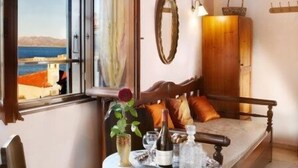A cozy room with a bed, a small table with a vase, and a view of the sea. - Archontiko Evgenia (Chania)