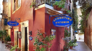 A narrow street with a red building featuring a blue sign for 'Arhontiko Evgenia'. - Archontiko Evgenia (Chania)