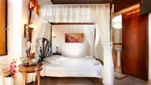 A four-poster canopy bed with white linens, a bedside table with a lamp, and a painting on the wall. - Archontiko Evgenia (Chania)