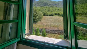 A window with a green frame, offering a view of a green landscape with trees and hills. - Hotel Spiridoula (Konitsa)