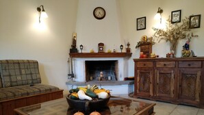 A living room with a fireplace, a sofa, a coffee table with decorative items, and a cabinet with framed pictures. - Hotel Spiridoula (Konitsa)