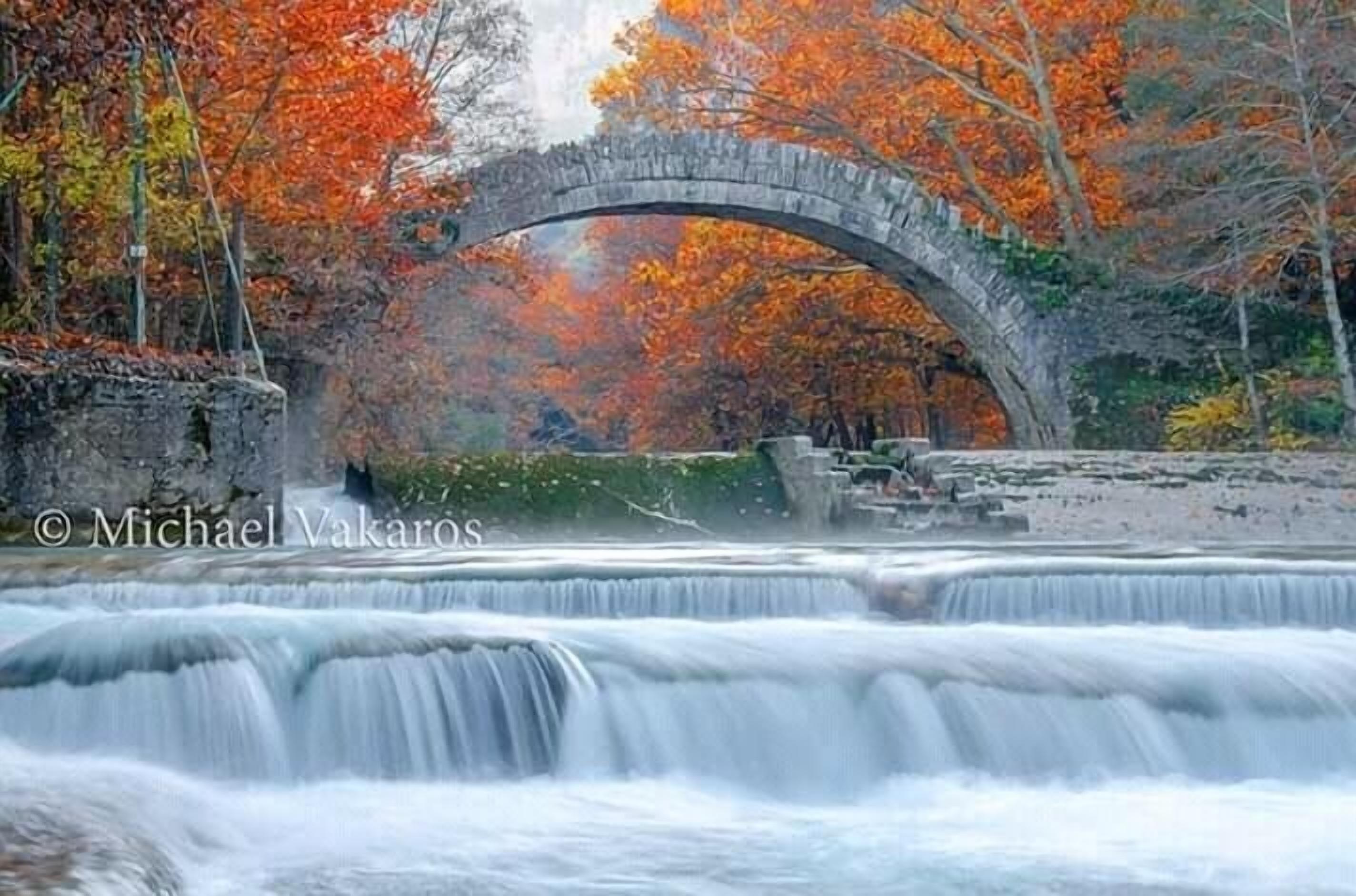 Eine Steinbrücke über einem Wasserfall, umgeben von Herbstlaub.