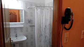 Un baño con lavamanos, cortina de ducha con estampado floral y teléfono fijo en la pared.