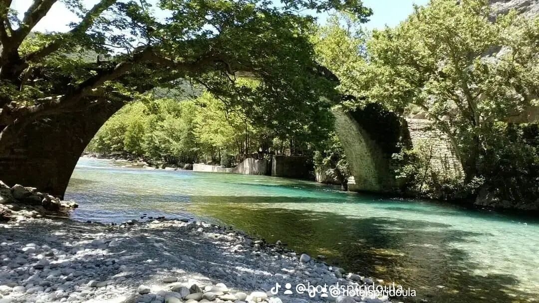 Un puente de piedra sobre un río claro, rodeado de árboles y terreno rocoso.