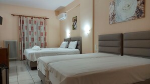 A hotel room with two beds, a radiator, a desk, and a wall-mounted air conditioner. - Hotel Spiridoula (Konitsa)