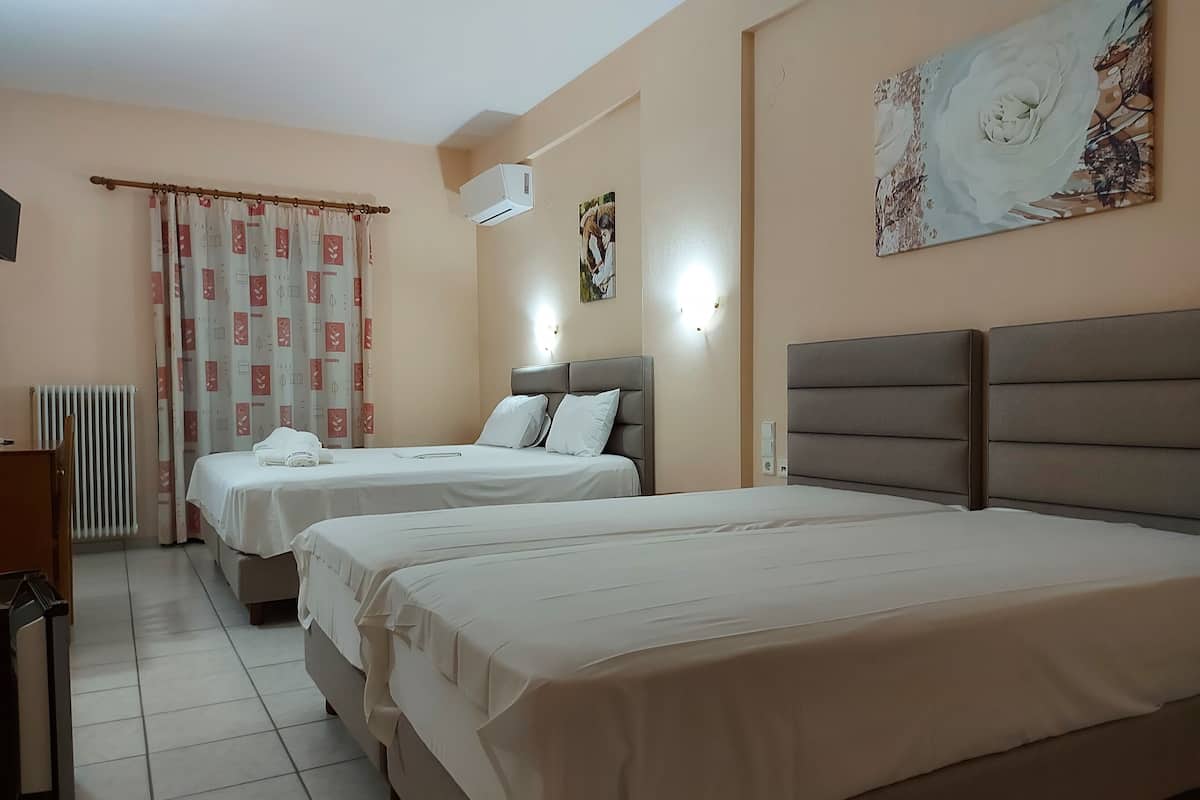 A hotel room with two beds, a radiator, a desk, and a wall-mounted air conditioner.