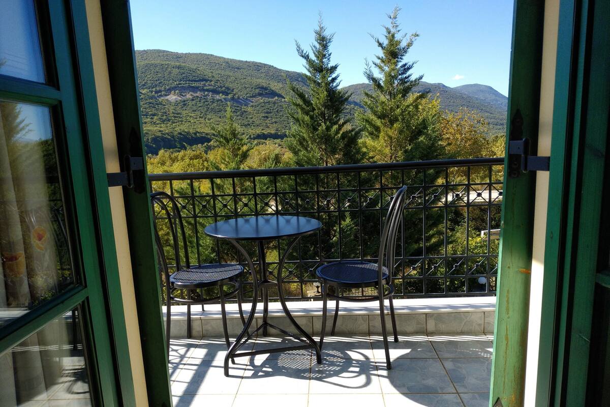 A balcony with a table and chairs, offering a view of a mountainous landscape.