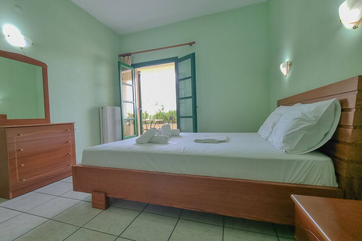 A bedroom with a bed, wooden dresser, and a view through an open door.
