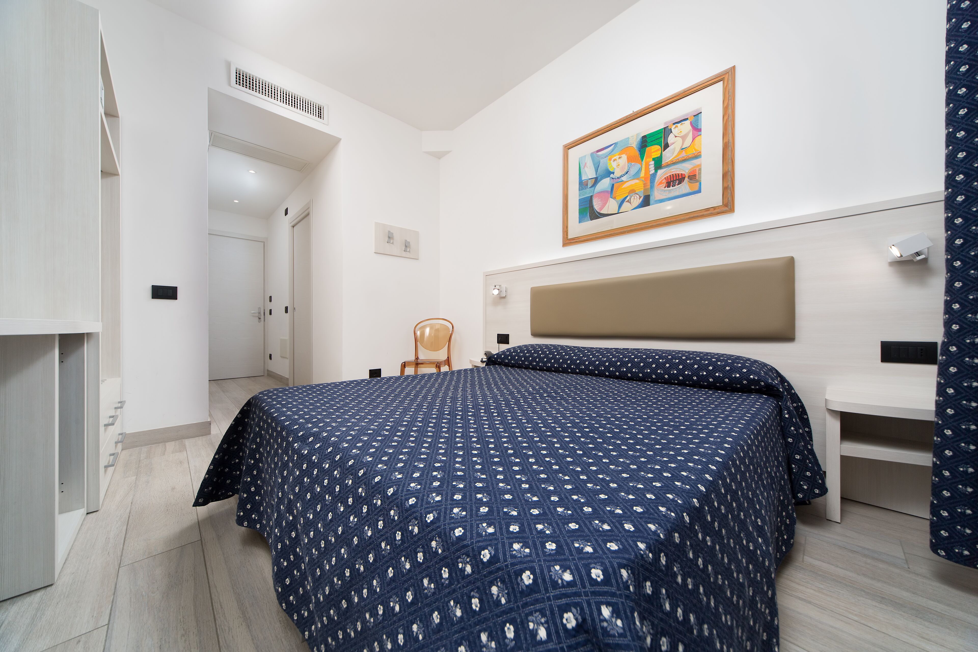 Un dormitorio con cama, una silla, un escritorio y un cuadro en la pared.
