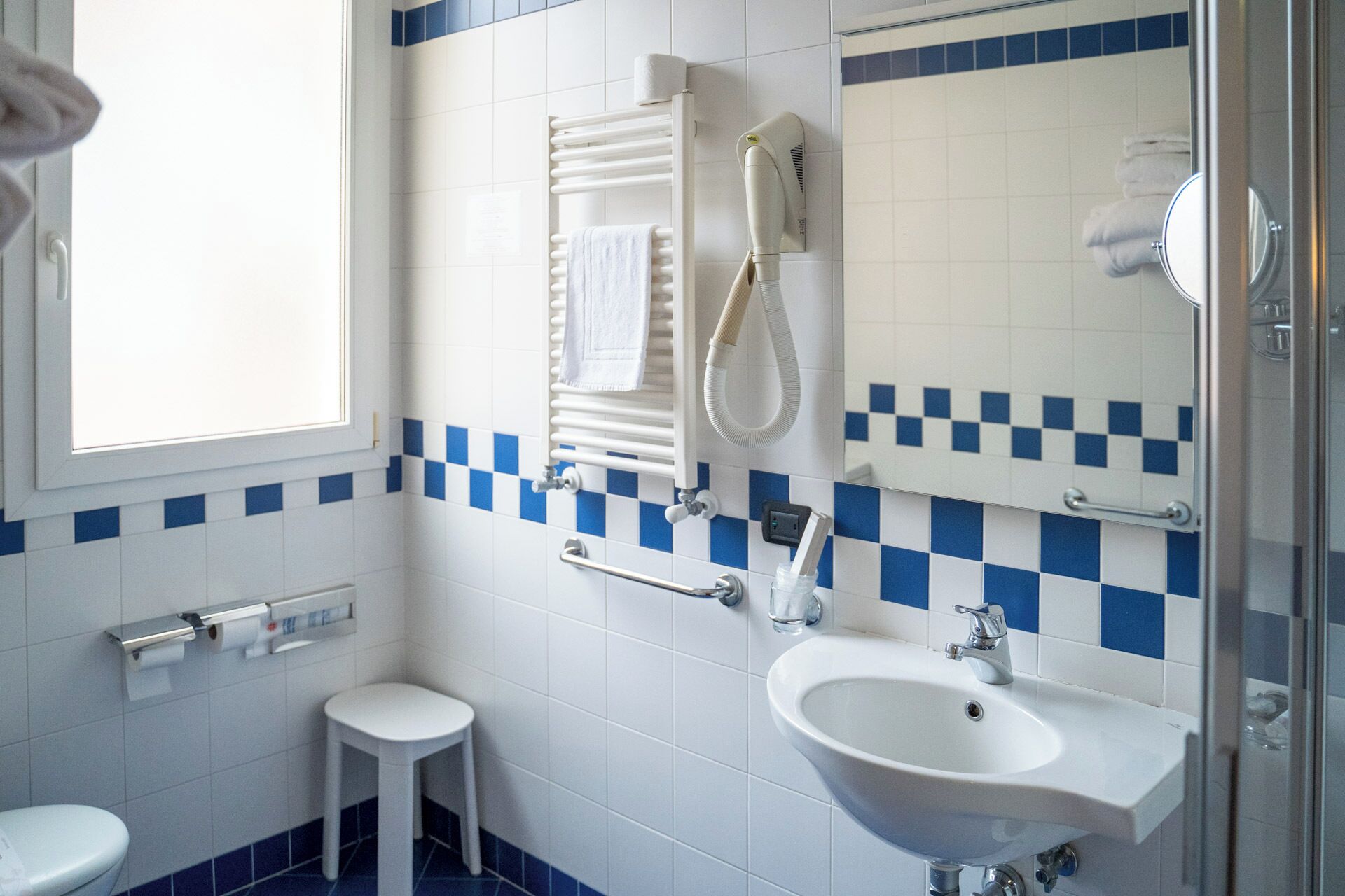 A bathroom with a white sink, a handheld showerhead, a towel rack, and a toilet.