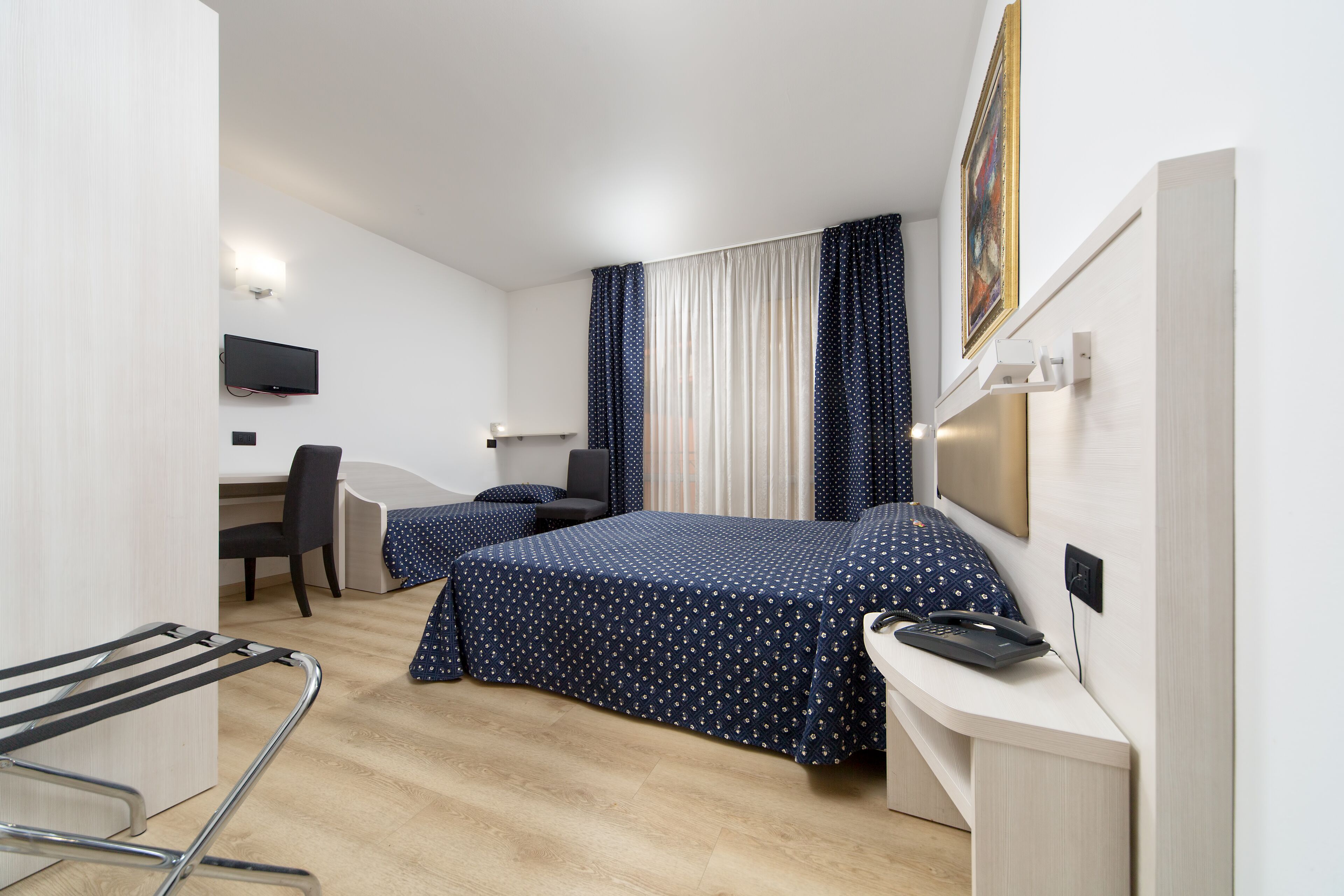 Une chambre d’hôtel avec deux lits, un bureau, une chaise et un téléviseur fixé au mur.