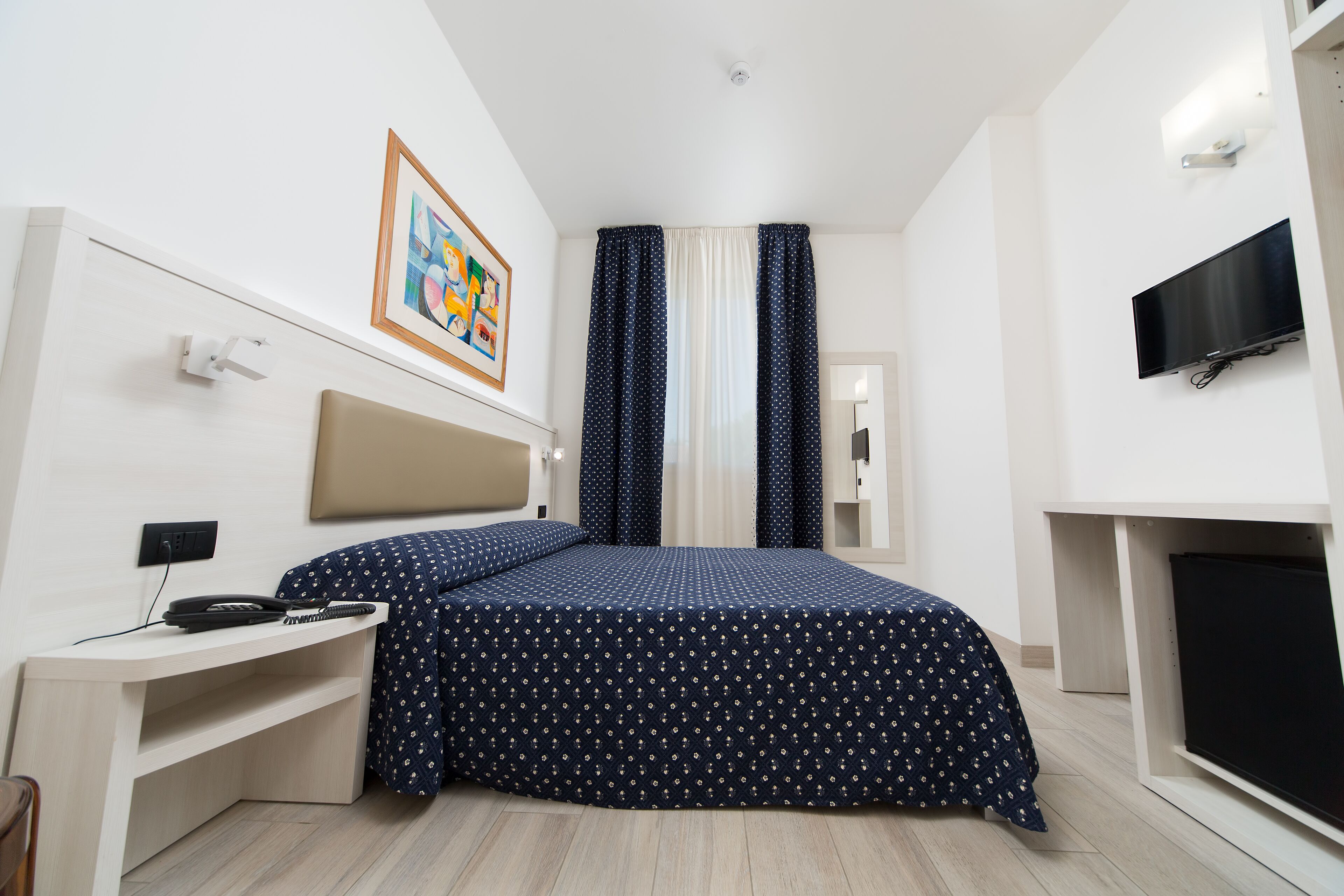 Una habitación de hotel moderna con una cama, un escritorio, un televisor y un cuadro en la pared.