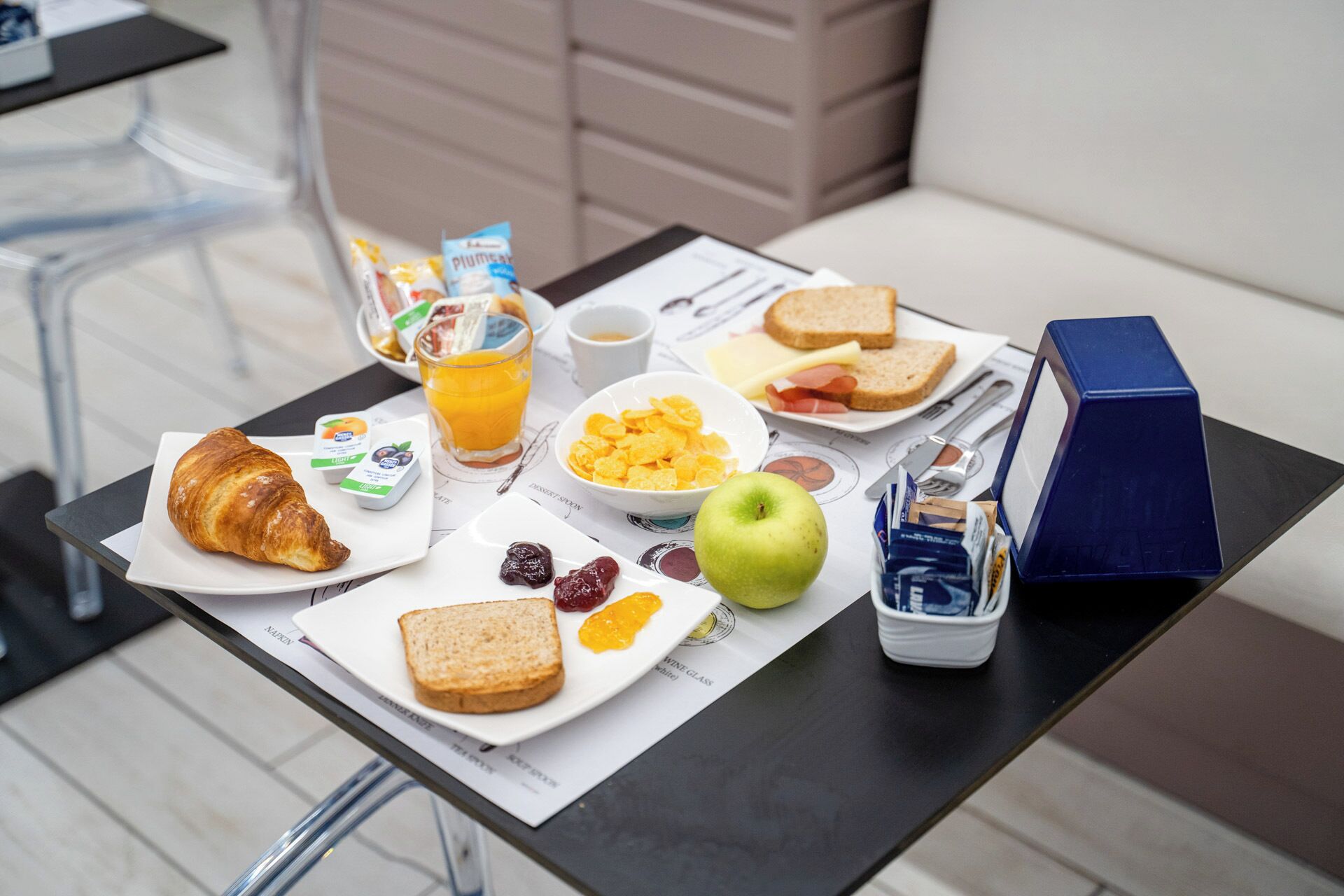 Een ontbijttafel met croissants, cornflakes, fruit en sap.