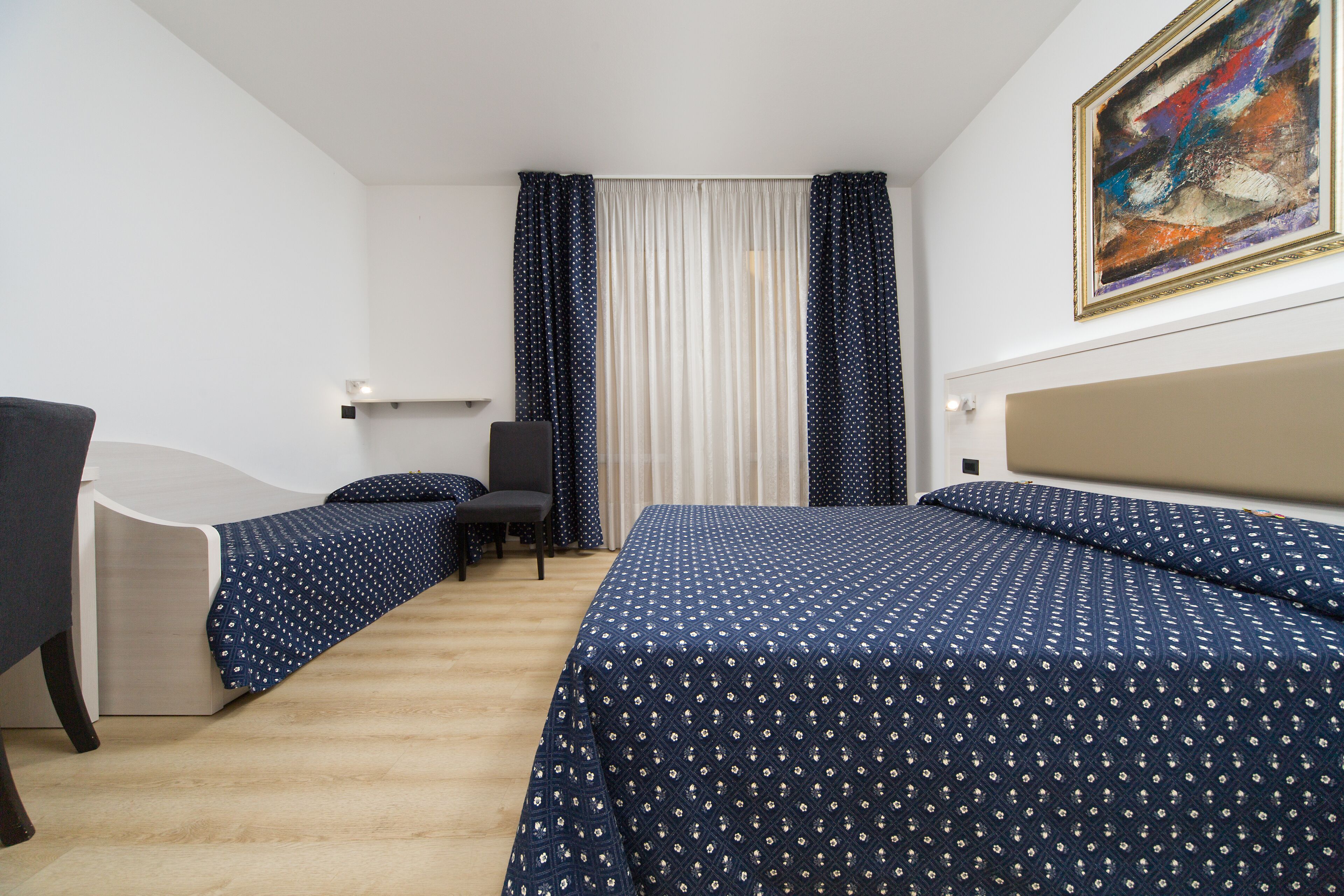 Ein Hotelzimmer mit Bett, Stuhl, Schreibtisch und einem Bild an der Wand.