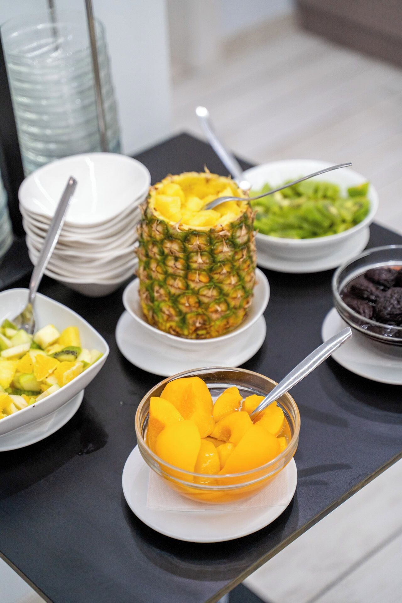 A buffet table with various fruit dishes, including pineapple, kiwi, and peaches.